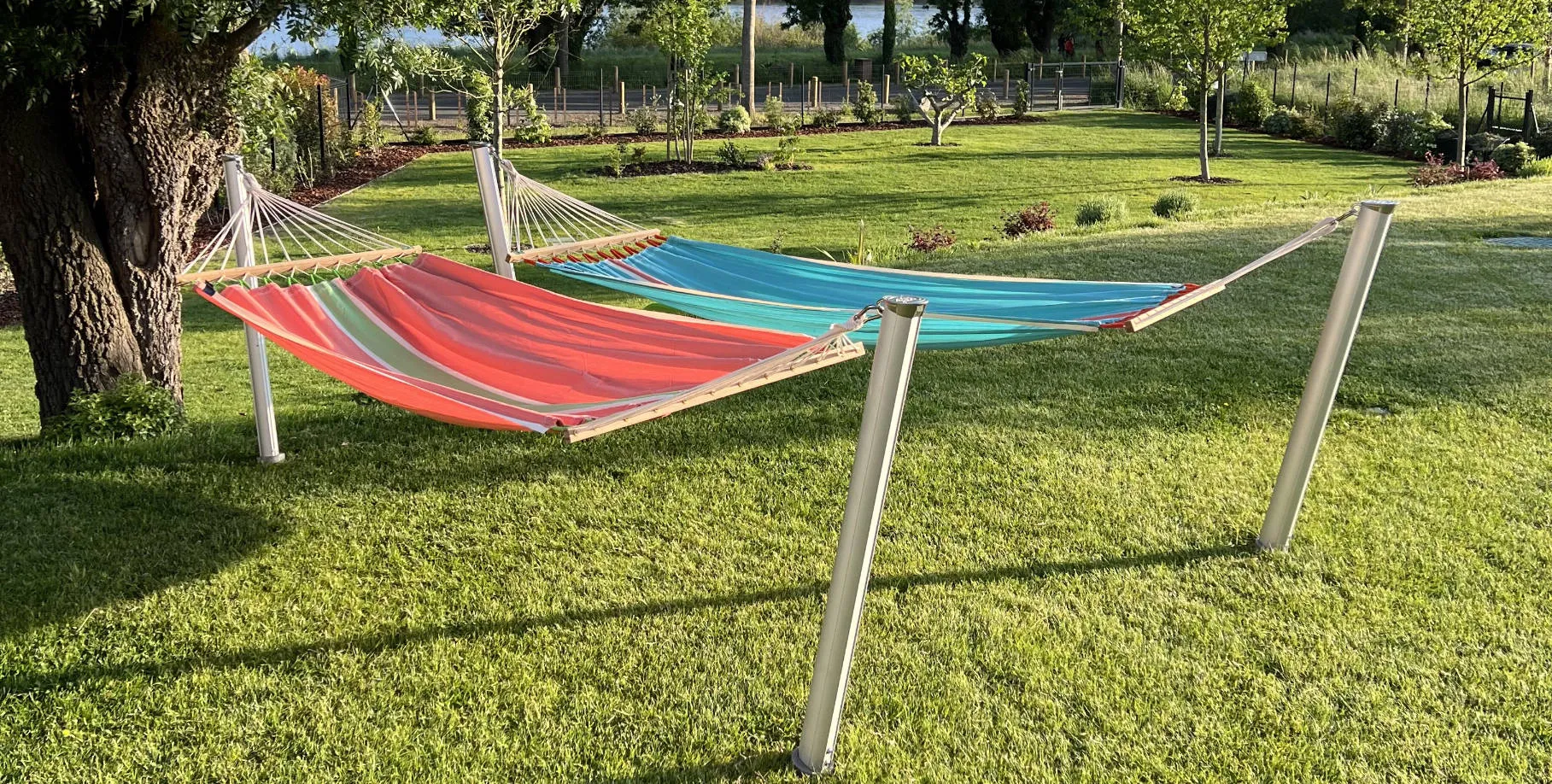 deux hamacs colorés supportés par quatre poteaux Gard&Rock dans un jardin verdoyant au bord de la rivière, coin détente idéal